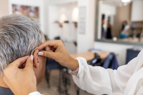 Audiologist fitting a hearing aid on a man's ear